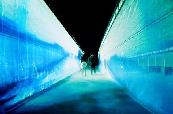 54: Manchester's installation in the Warehouse. It shows two people walking through a fabric walkway, which is illuminated by blue lights.