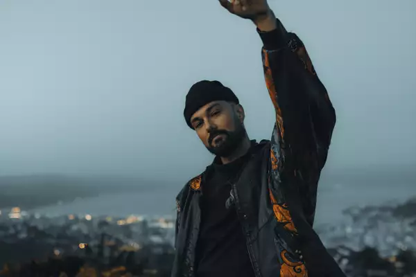 Photo of Rei with his arm in the air wearing a black hat and jacket