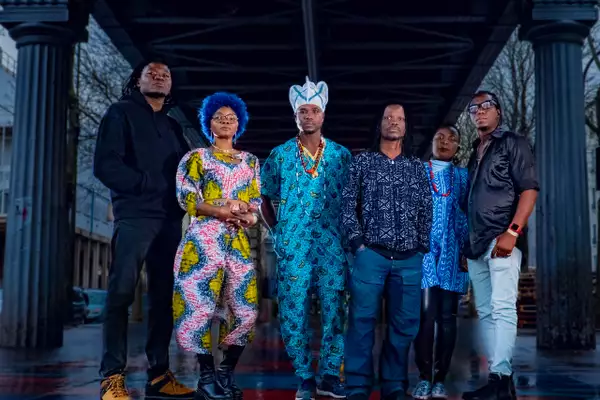 Six members of BIM stood outside under a bridge, wearing bright, patterned clothing