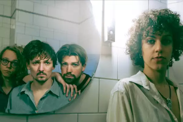 Photograph of the four members of Ão. Three are reflected in a mirror. The other is standing next to the mirror.