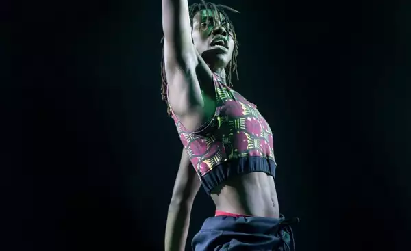 A photograph of a dancer stretching their right arm out of the top of the frame