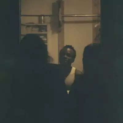 Sepia photo of Iyunoluwa Yemi-Shodimu stood between the shadows of two people