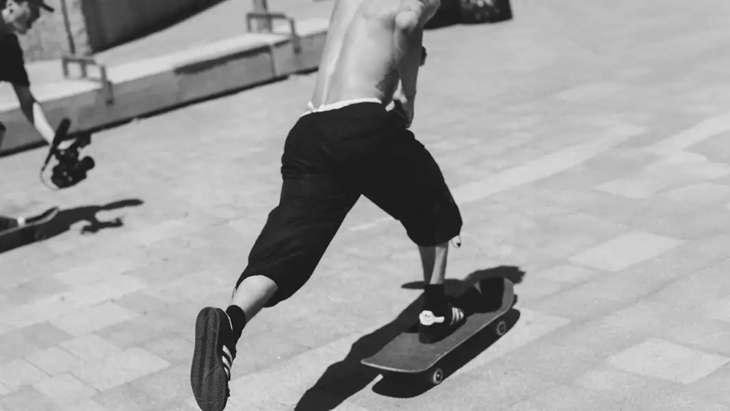 Black and white photograph of a skateboarder skating wearing black adidas trainers
