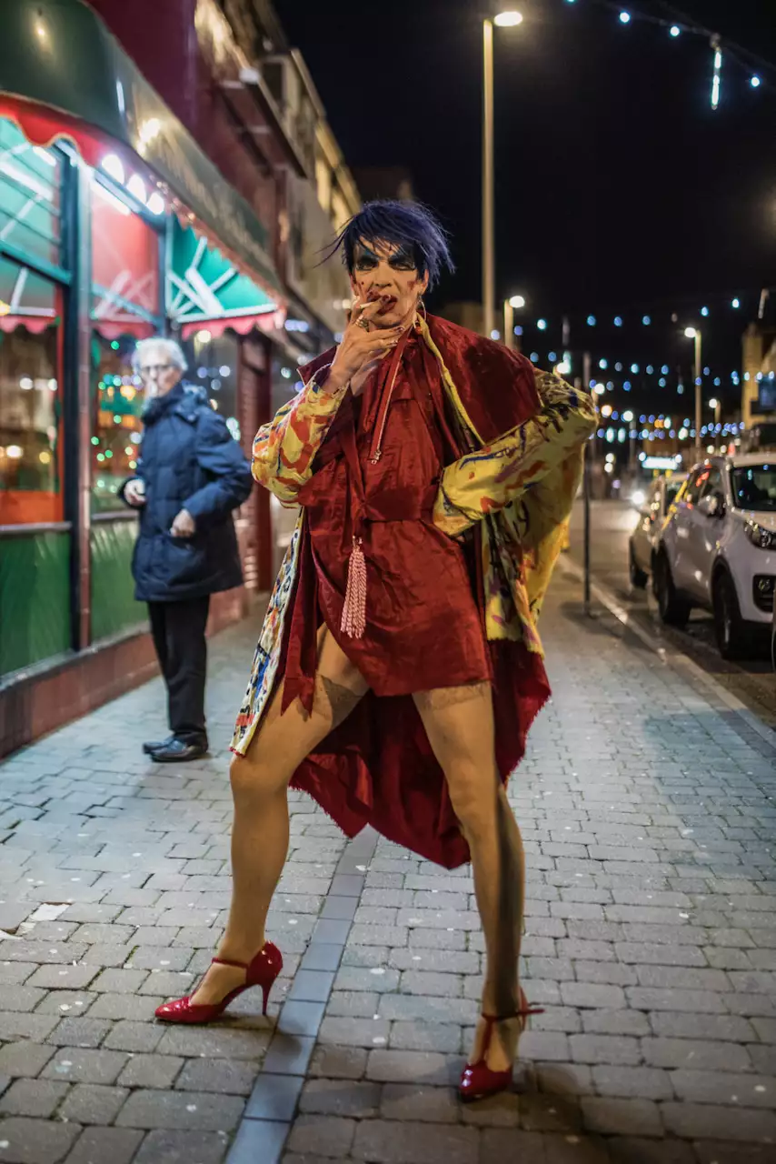 David Hoyle with blue hair and a red dress, stood on a street at night smoking a cigarette