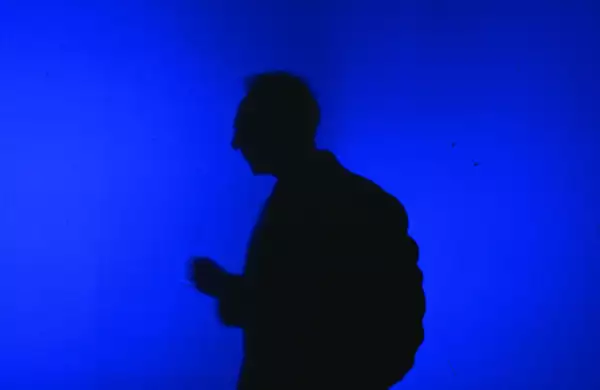 Silhouette of a person against a vibrant blue background. There is a stark contrast between the dark shadow and the bright blue backdrop.