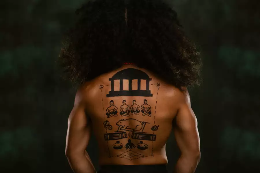 A member of FAFSWAG with their back turned away from the camera. They are topless with hand-drawings on their back. The background is dark green.