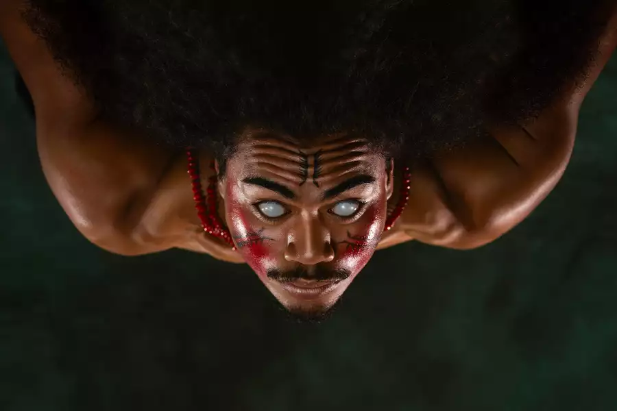 A member of FAFSWAG with glowing white eyes and red and black face paint stares intensely at the camera. They wear red beaded necklaces, and the image is flipped upside down.