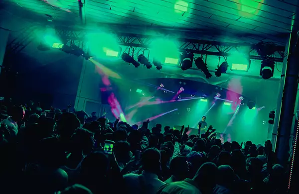A DJ set on Festival Square from MIF23, showing a large crowd of people dancing and filming a DJ on stage. The lighting is hazy green and there are purple strobe lights.