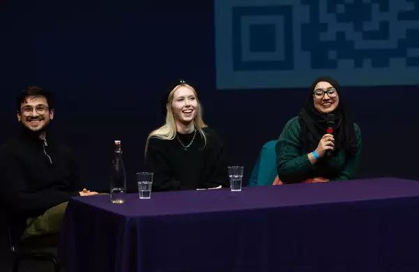 Three people smiling during a panel talk. One is speaking into a microphone.