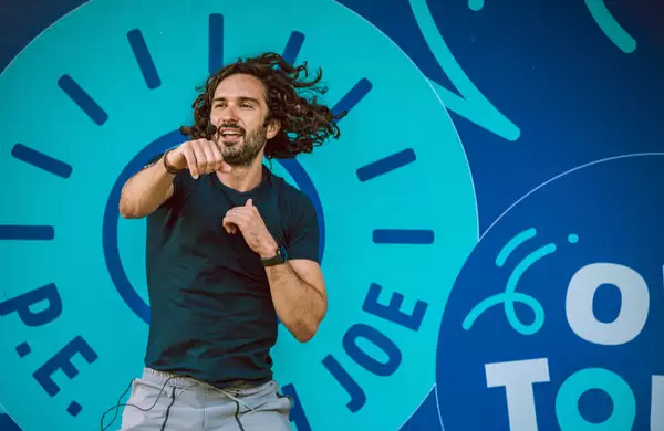 Joe Wicks leading a workout in front of a sign that says 'P.E. with Joe'
