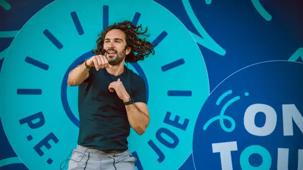 Joe Wicks leading a workout in front of a sign that says 'P.E. with Joe'