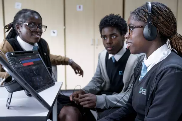 Three children sat around an iPad, one wearing headphones