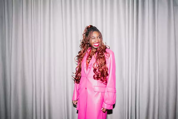 Factory+ Editor in Residence Kemi Alemoru wears a pink trench coat and smiles at the camera