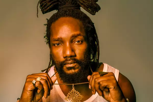 Kabaka Pyramid wearing a white vest and gold chain
