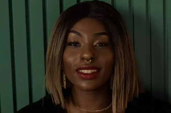 A young woman wearing red lipstick and a septum piercing smiles at the camera.