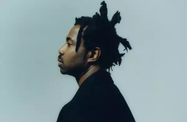 Side angle of Sampha on a light blue background