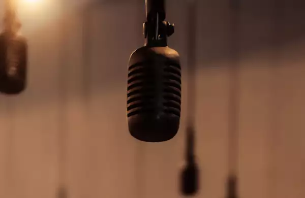 A close-up of a microphone hanging from above, with several similar microphones blurred in the background. The warm lighting and soft focus create an atmospheric feel.