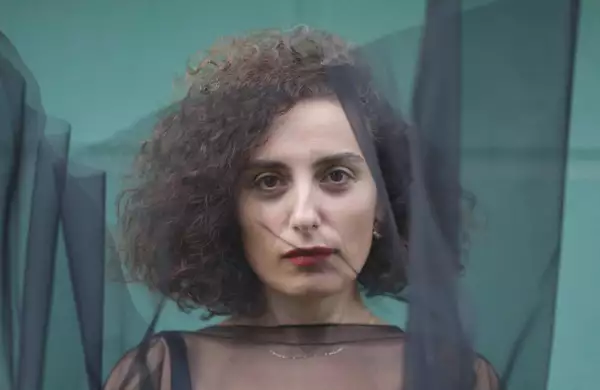 Sanem Kalfa stood in front of a turquoise wall, with a black transparent piece of material covering her face