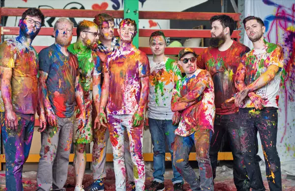 Nine members of Young Pilgrims covered in colourful paint, posing in an artistic setting.