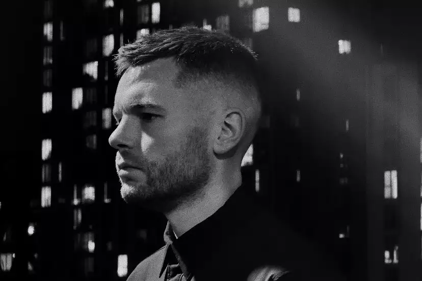 Black and white photo of Ewan Sim looking to the side. In the background is a blurry skyscraper.