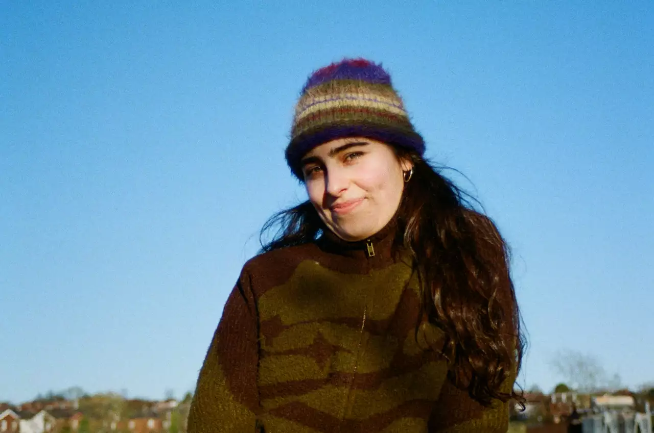 Zuri sat outside wearing a woollen striped hat and coat. It is a clear, sunny day.