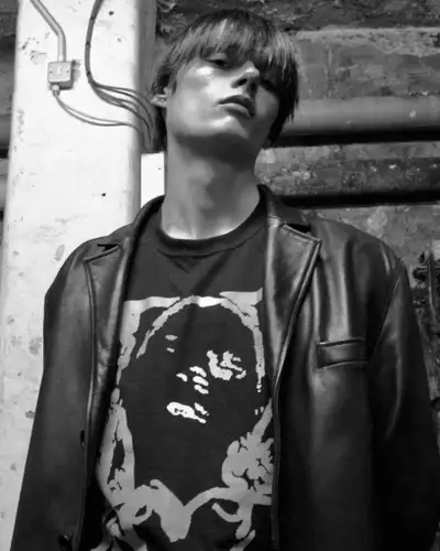 Black and white photo of Gabriel Evans wearing a black leather jacket and looking down at the camera