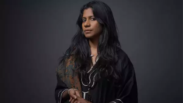 Headshot of ganavya wearing a black shirt and patterned brown scarf on a black background